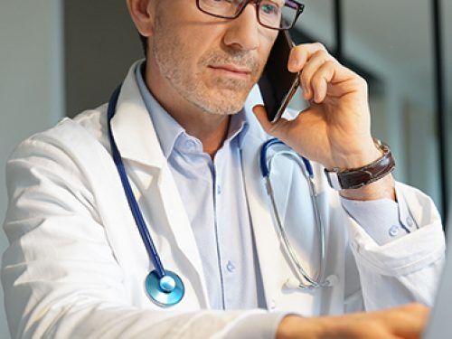 Lekarz rozmawia przez telefon oraz pisze na laptopie