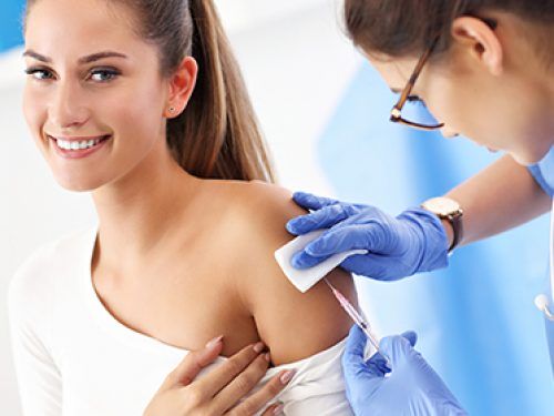 Lekarka wykonuje uśmiechniętej kobiecie szczepienie w ramię